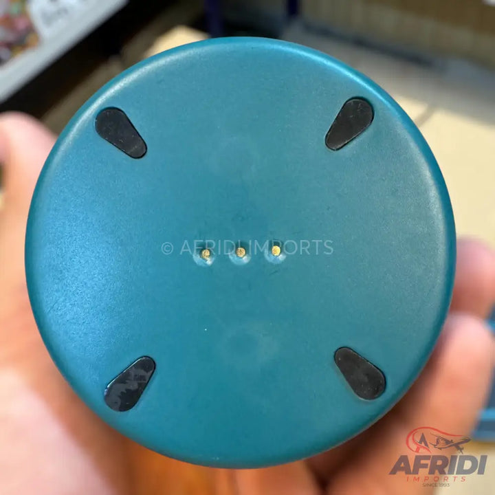 The bottom of a teal-colored cylindrical device with four black rubber feet and three metallic charging pins.