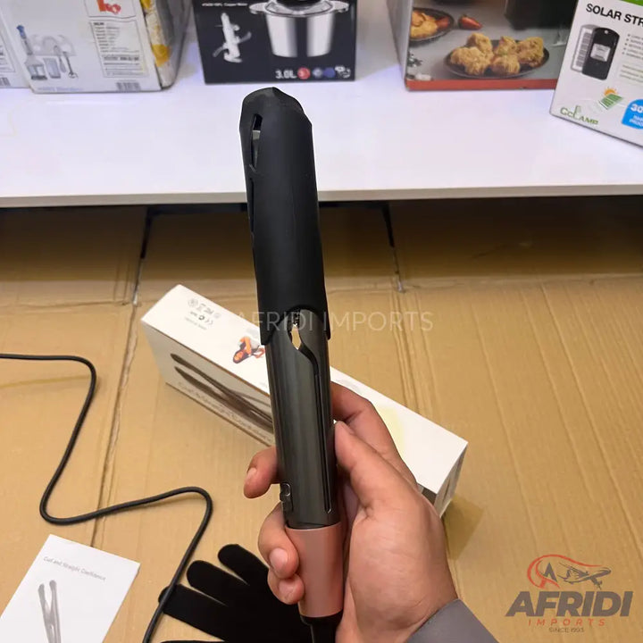 A dark grey and rose gold automatic hair curler with a black protective top, held by a hand.