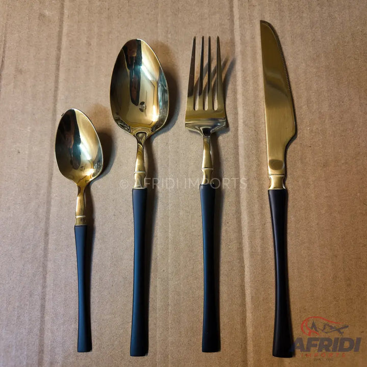A four-piece set of gold-colored flatware with black handles.