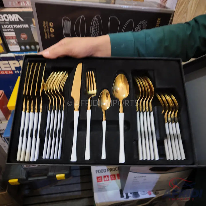 A cutlery set with gold-colored tops and white handles, neatly arranged in a black presentation box.