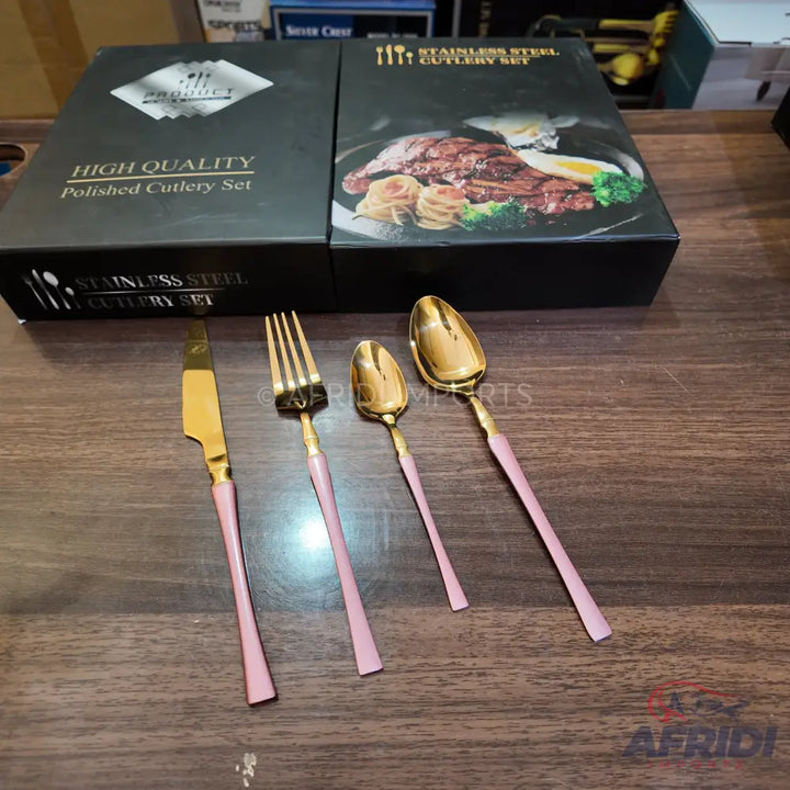 A four-piece set of gold-colored stainless steel cutlery with pink handles, presented in two black gift boxes.