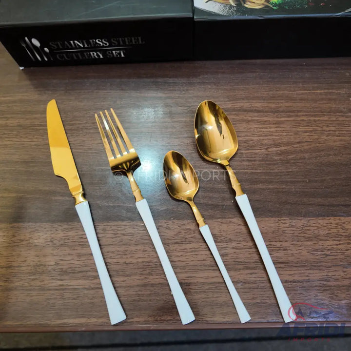 A four-piece set of gold-colored stainless steel cutlery with white handles.