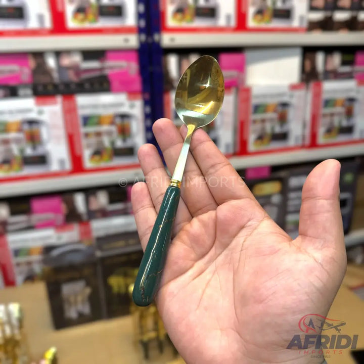 A gold-colored spoon with a dark green handle.
