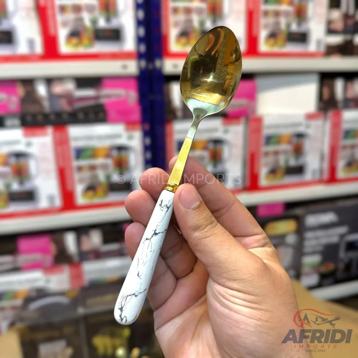 A gold-colored spoon with a white marble-patterned handle.