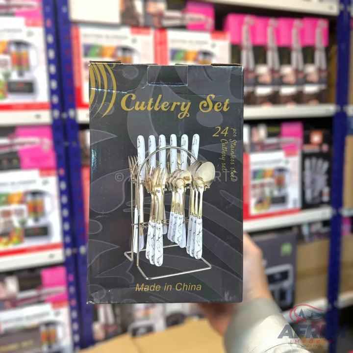 A 24-piece cutlery set with gold-colored tops and white, marbled handles, displayed on a metal stand.