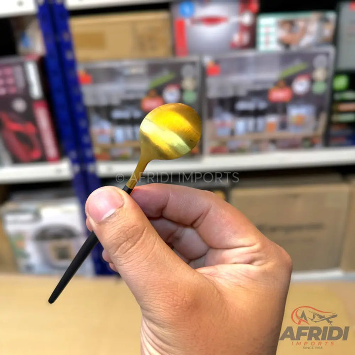 A gold-colored miniature spoon with a black handle.