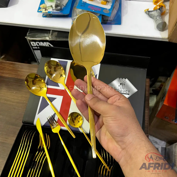 A set of gold-colored metallic cutlery, including spoons, forks, and knives.