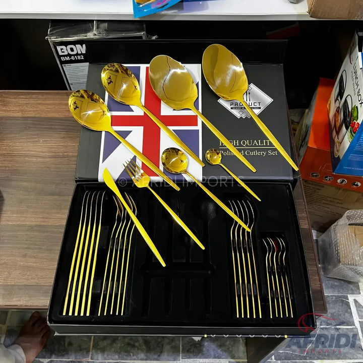 A gold-colored cutlery set, including spoons, forks, and knives, in a display box featuring a Union Jack design.