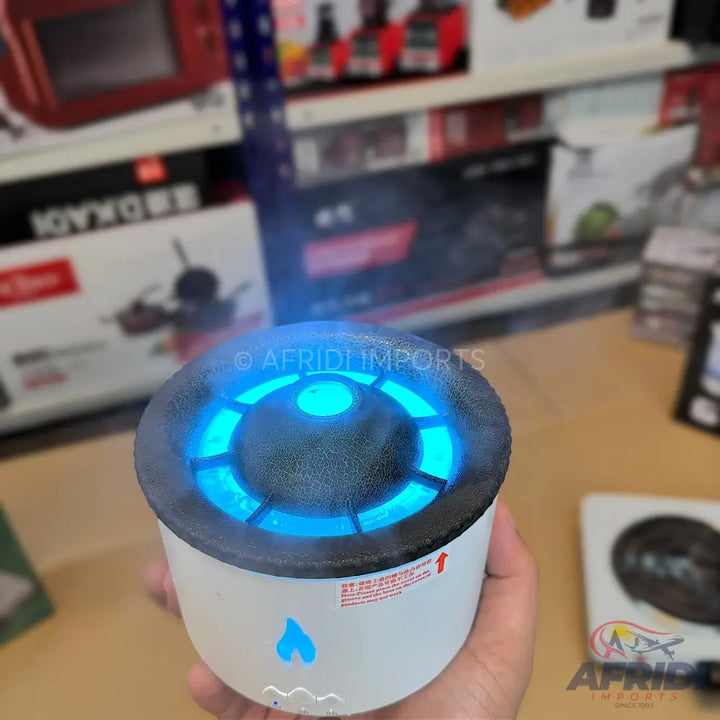 A white, cylindrical humidifier or air diffuser with a black top that emits blue light and a fine mist.
