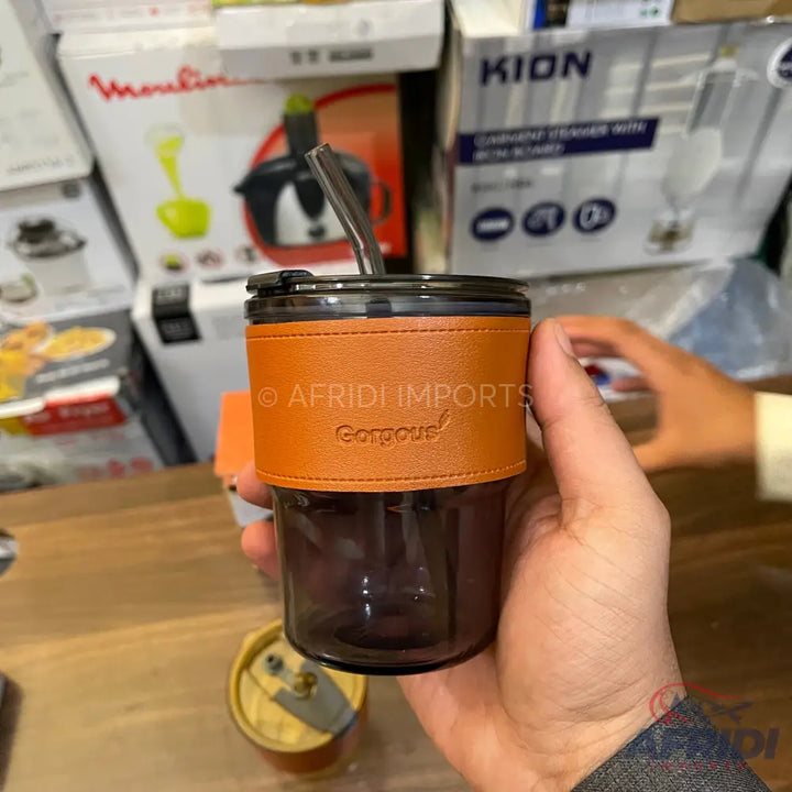 Dark glass tumbler with a brown leather-like sleeve and a metal straw.