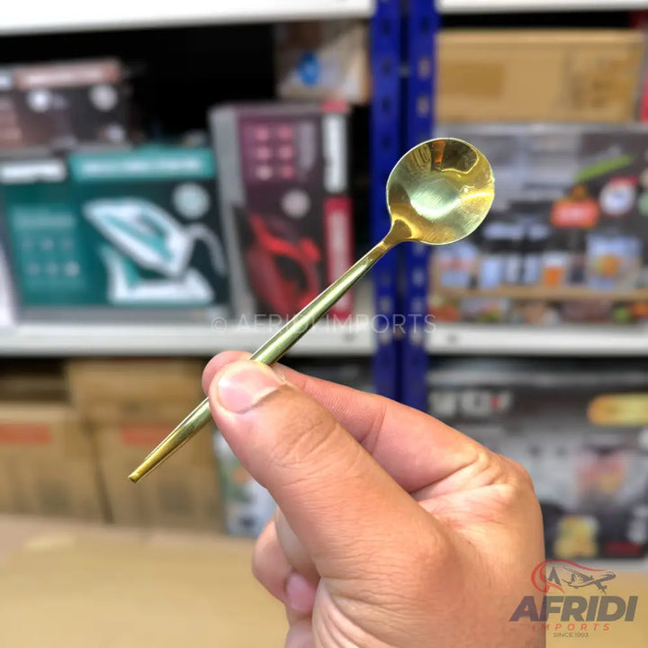A small, golden metal spoon with a slender handle.