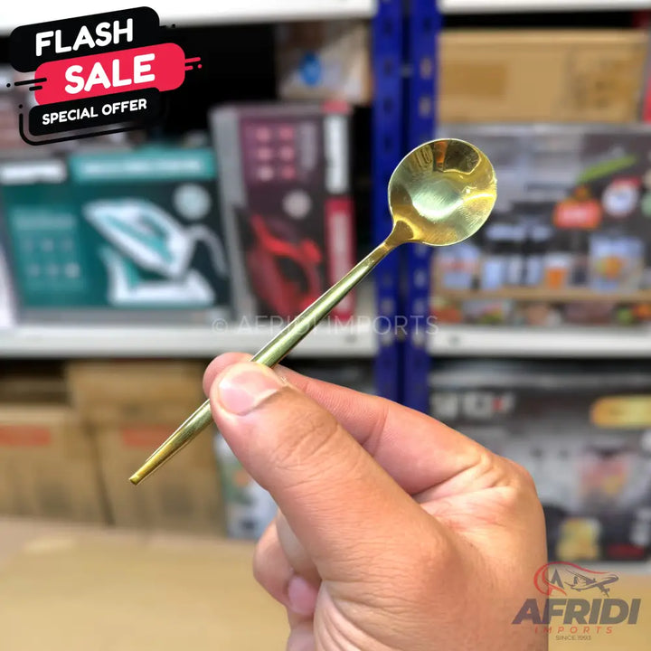 A small, golden metal spoon with a slender handle.
