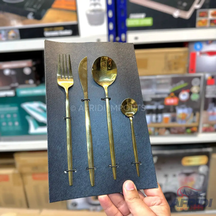 A set of four golden-colored eating utensils, including a fork, knife, large spoon, and small spoon, displayed on a dark rectangular card.