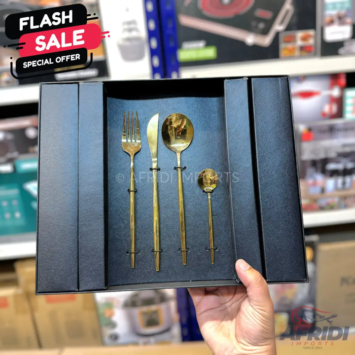 A four-piece set of golden-colored cutlery, including a fork, knife, large spoon, and small spoon, presented in a black gift box.