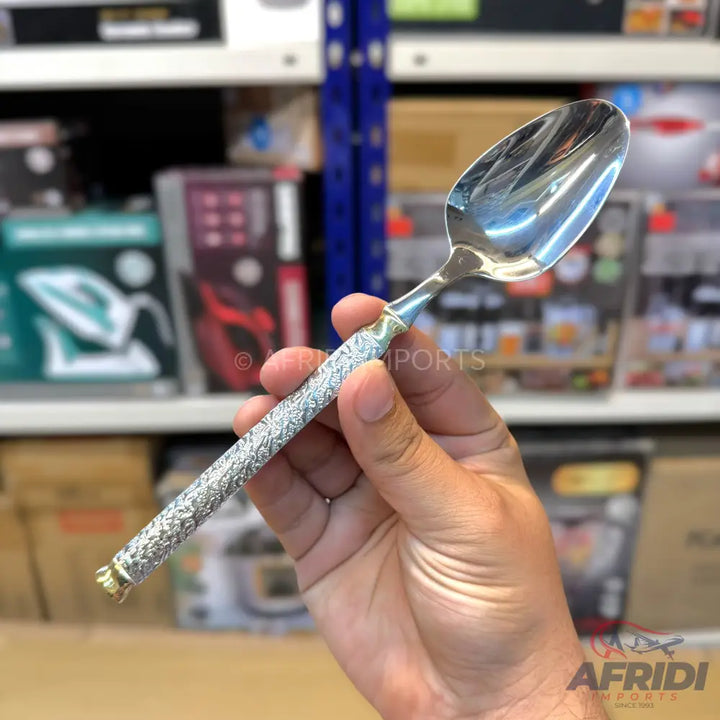 Silver-colored spoon with an ornate, textured handle and a gold-colored tip.