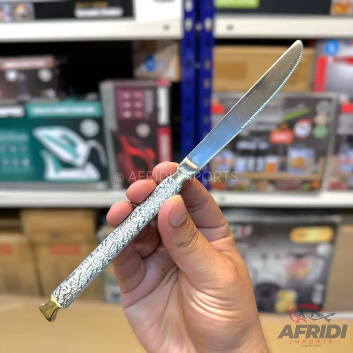 A silver-colored butter knife with an intricately patterned handle and a golden end cap.