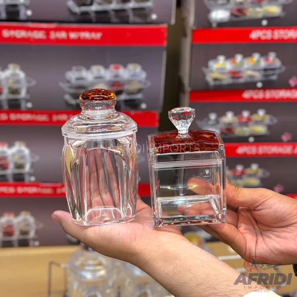 Two clear glass storage jars with decorative lids, one round and one square.