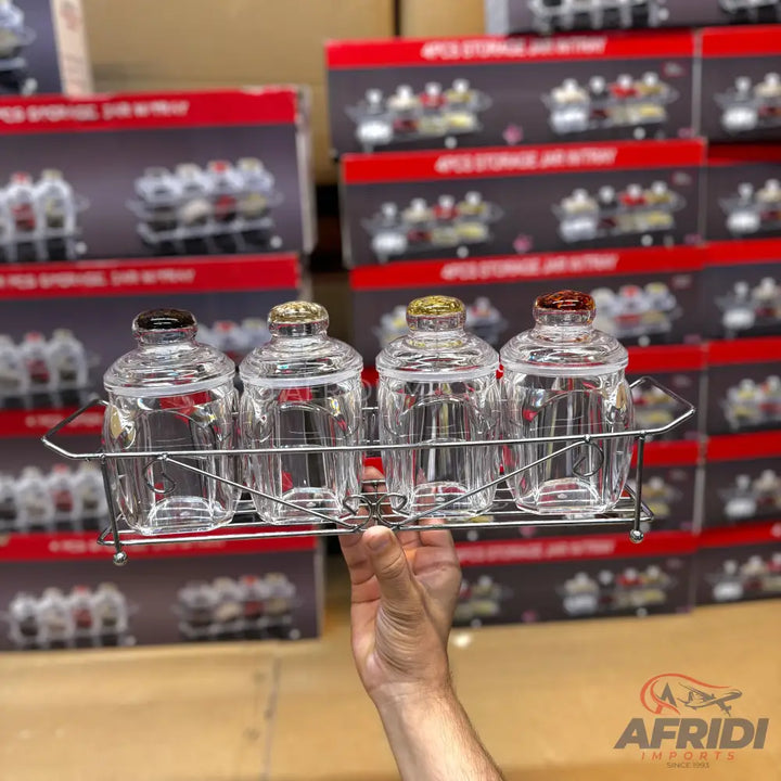 A set of four clear glass storage jars with colorful lids in a metal caddy.