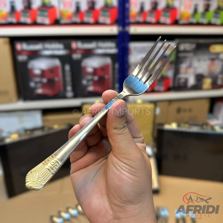 A silver-colored metal fork with an ornate, gold-colored handle design.
