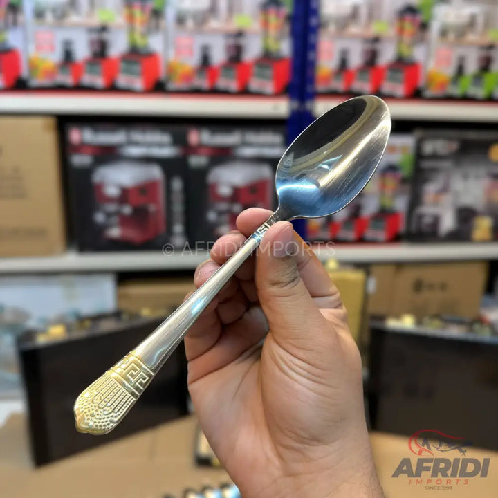Shiny silver metal spoon with a gold-colored, patterned handle tip.