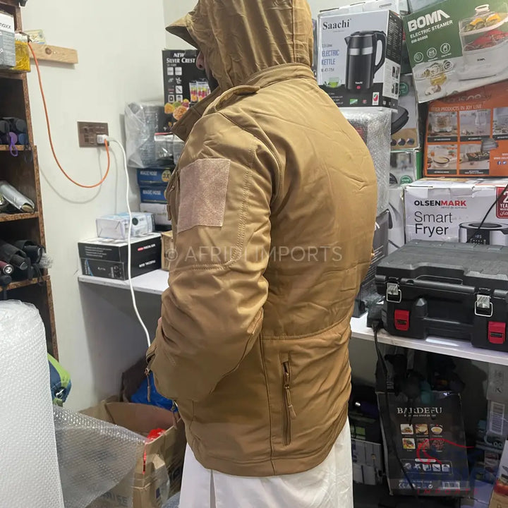 A person wearing a hooded brown jacket with a hook-and-loop patch on the upper arm.