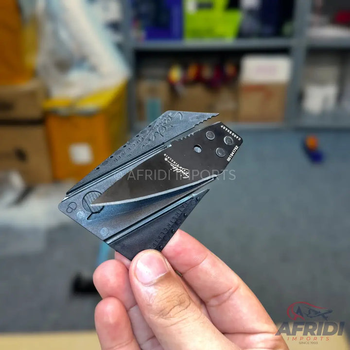 A credit card-sized, black, foldable utility knife with a serrated edge and various tools.