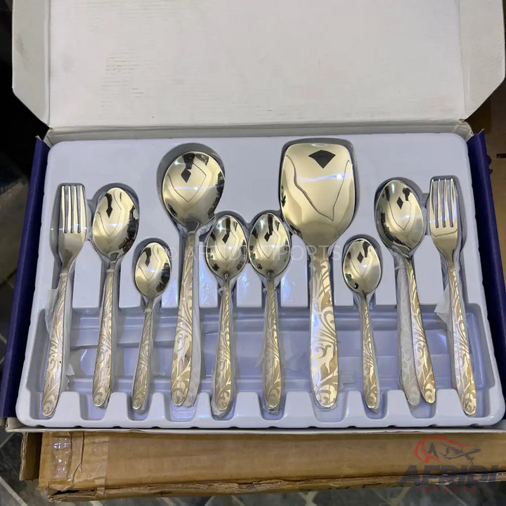 A boxed set of eleven ornate, silver-colored metal utensils, including forks, spoons, and a serving spoon.
