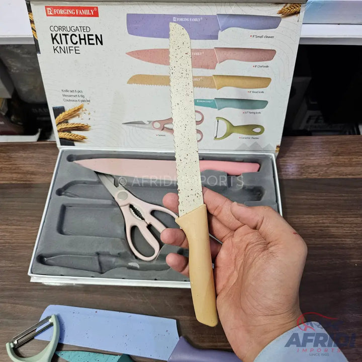 A set of kitchen knives and tools, including a bread knife, chef’s knife, utility knife, paring knife, kitchen shears, and a peeler, in varying pastel colors.