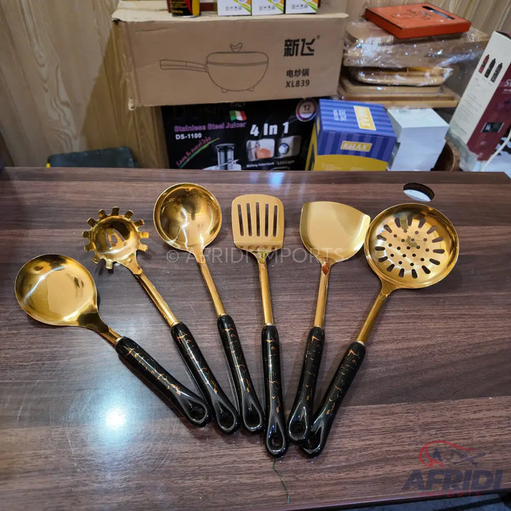 A set of six golden kitchen utensils with black handles.