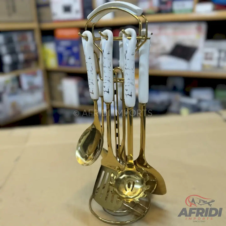 A golden kitchen utensil set with white ceramic handles on a rotating stand.