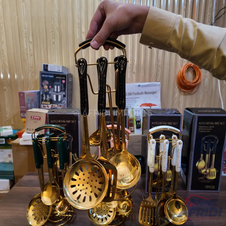 A set of gold-colored kitchen utensils with dark handles, displayed on a matching stand.