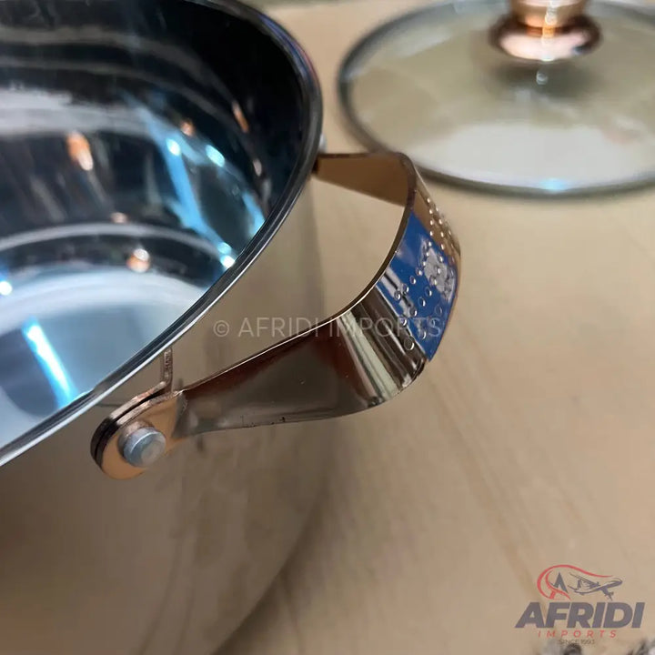 Stainless steel cooking pot with rose gold handles and a glass lid.