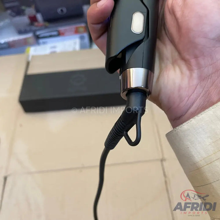 A person holding a black hair styling tool with a silver accent and a power cord.