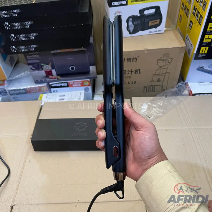 A black hair straightener with a power cord, held in a hand.