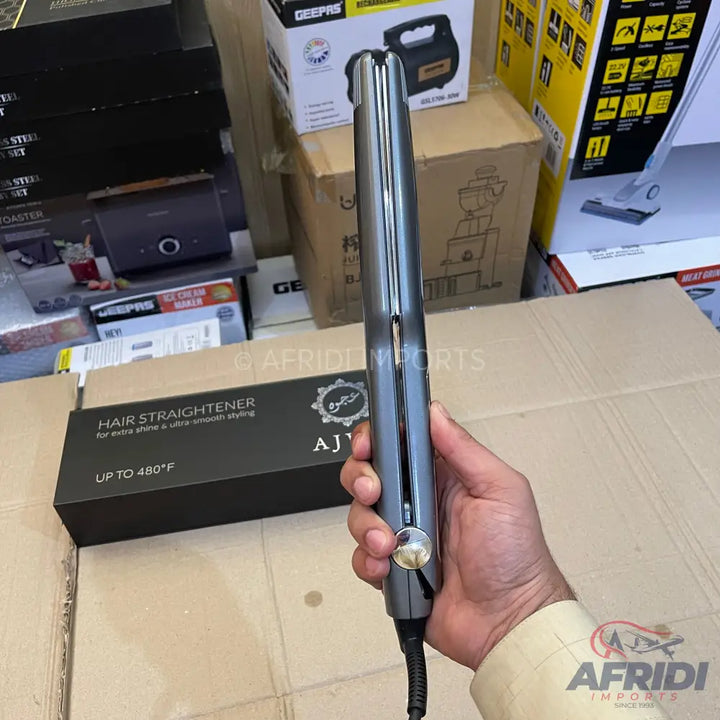 A dark gray hair straightener with a golden temperature control dial.