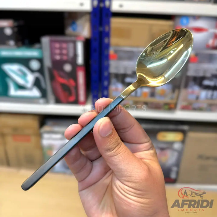 A hand holding a two-toned spoon with a golden bowl and a black handle.