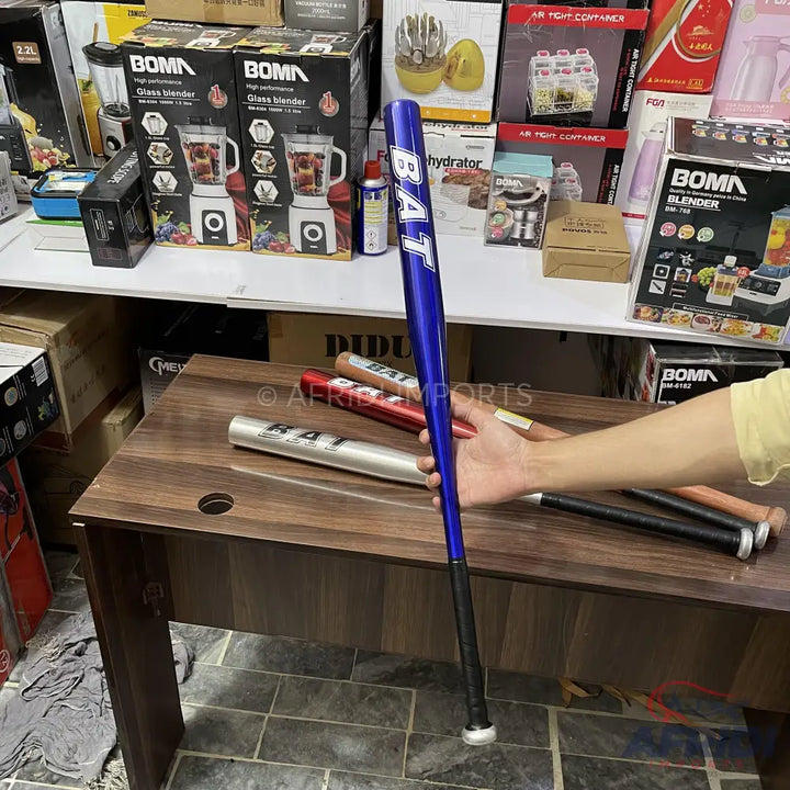 A person holding a blue metal baseball bat with a black grip, with other colored bats visible on the table.