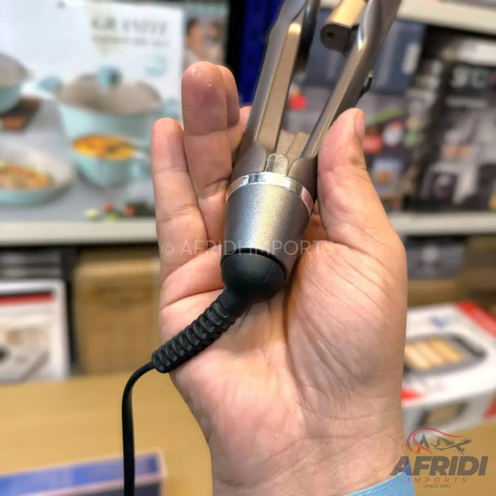 A hand holding a gray electric hair curler with a black power cord.