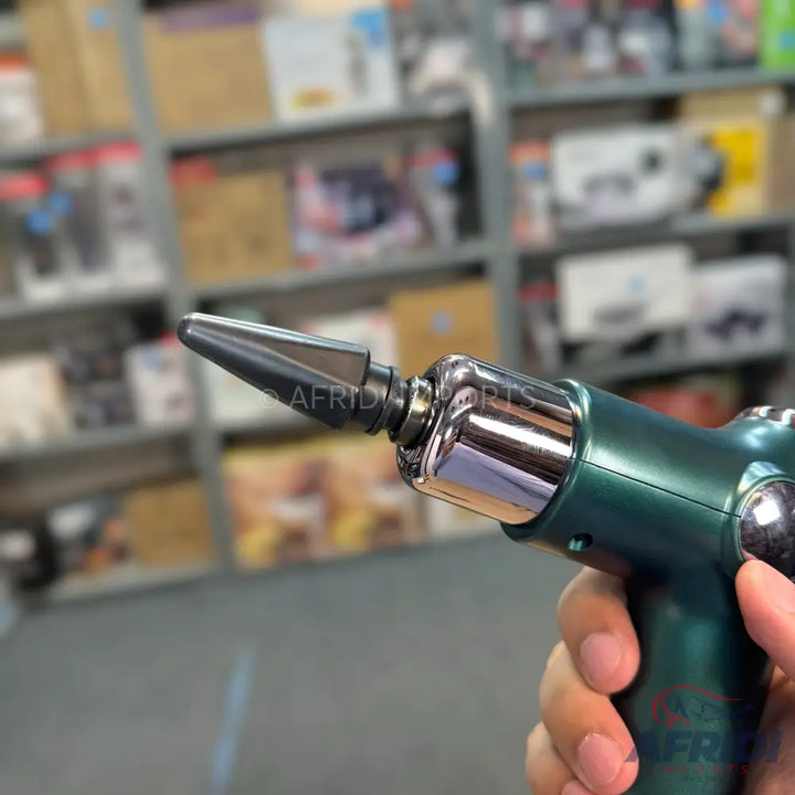A hand-held, dark green, metallic massage gun with a pointed black attachment.