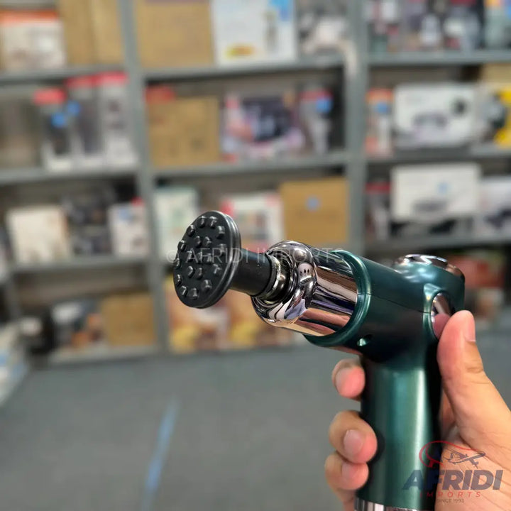 A handheld green and chrome massage gun with a multi-pronged head.