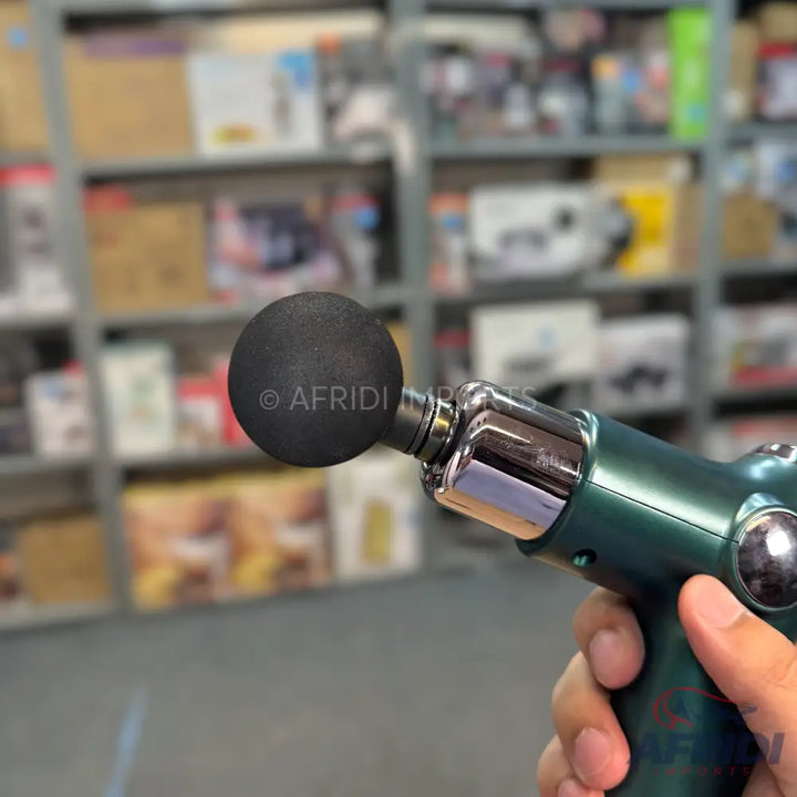 A handheld, dark green massage gun with a spherical black attachment.
