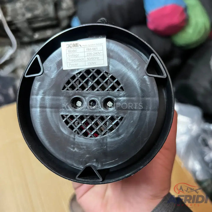 Bottom view of a black electric appliance with a ventilation grate and a label showing its model, voltage, frequency, and power.