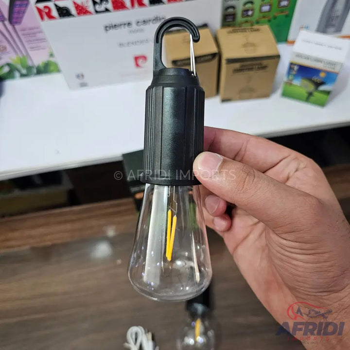 Hand holding a black, hook-top LED light bulb with a clear, pear-shaped glass casing.