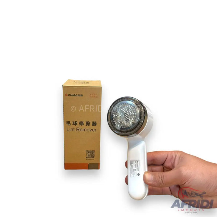 A white handheld lint remover with a clear circular head and a brown box.