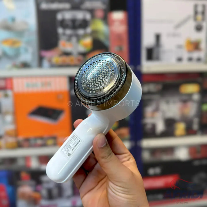 White handheld fabric shaver with a metallic gold ring around the perforated cutting head.