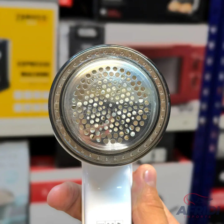 Handheld electric lint shaver with a perforated metal screen.