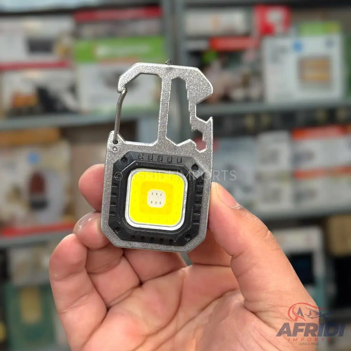 A silver multi-tool keychain with a bright yellow LED light.