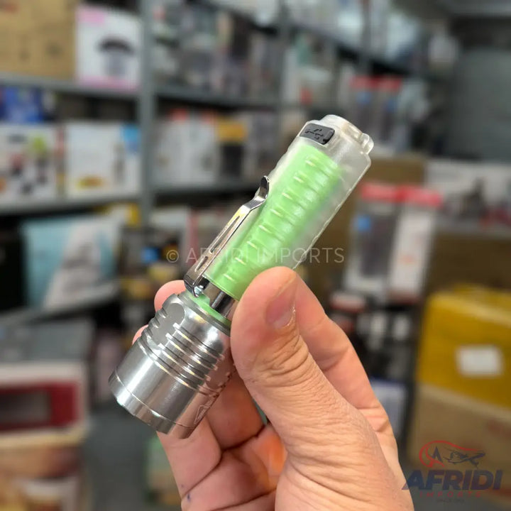 A hand holding a compact, clear-barreled flashlight with a visible green internal battery and a metallic base.