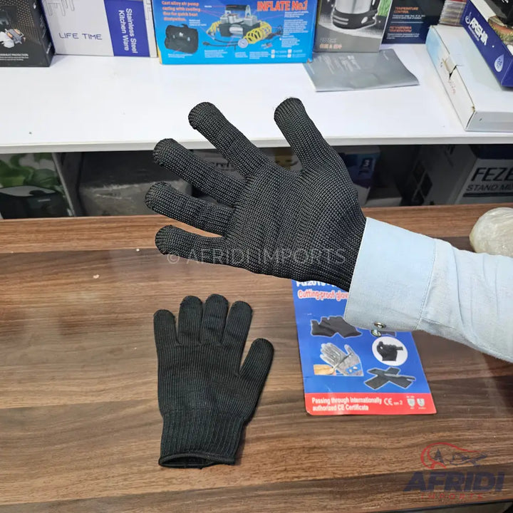 Two black cut-resistant safety gloves, one worn on a hand and one resting on a surface.