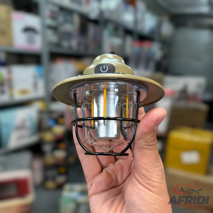 A small, portable lantern with a power button on top, featuring a clear casing with internal yellow-tinted light elements and a black wire cage.